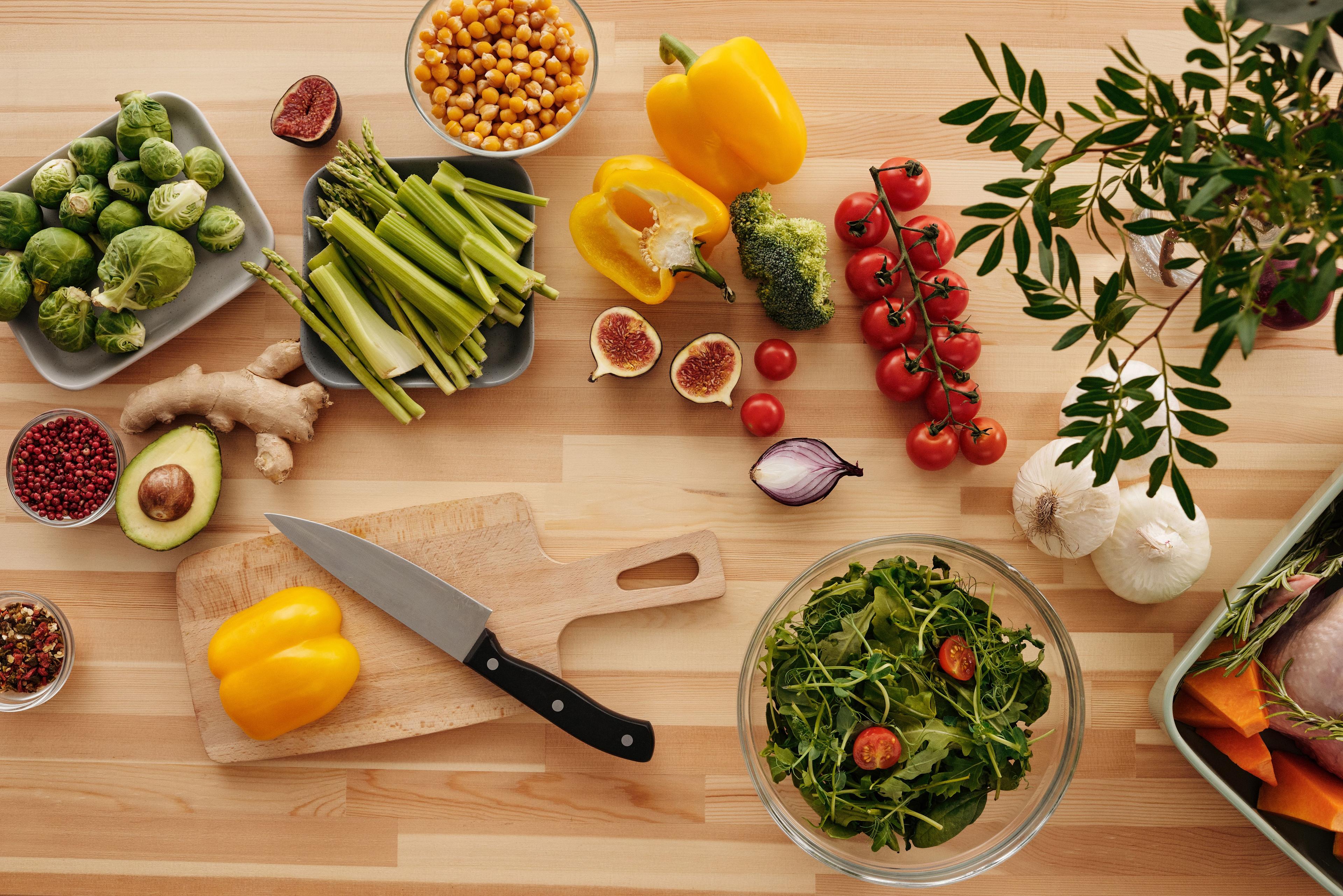 Fresh vegetables, chickpeas, fruit, herbs, and cooking ingredients arranged on a wooden table.